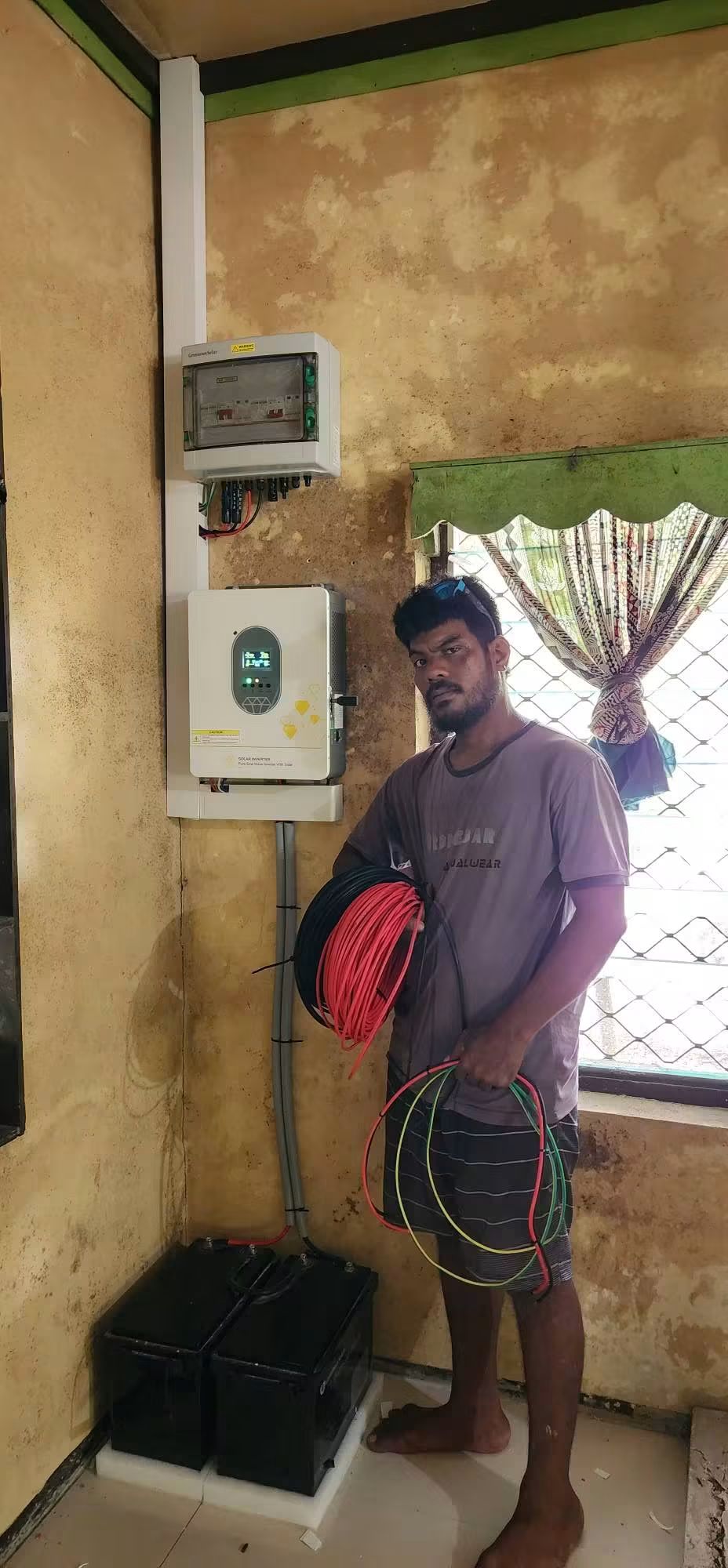 Installer holding cables beside a wall-mounted solar inverter